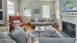 A living room with a fireplace, a map on the wall, and a cozy seating area. - Stylish In-Town Cottage- Walk to everything! (Vineyard Haven)
