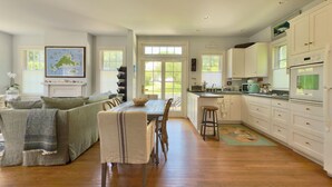 A spacious kitchen with white cabinets, a dining area with a wooden table and chairs, and a cozy living room with a sofa and decorative pillows. - Stylish In-Town Cottage- Walk to everything! (Vineyard Haven)