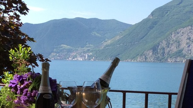 Ein Tisch mit einer Flasche und Gläsern, ein Stuhl und Blick auf einen See und Berge.