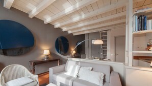Ein Wohnzimmer mit Sofa, Sessel und Couchtisch. Ein Bücherregal mit Büchern und eine Lampe auf einem Beistelltisch.