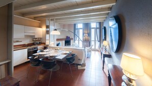 Eine moderne Küche mit weißen Schränken, einer Essecke mit Tisch und Stühlen sowie einem großen Fenster mit Vorhängen.