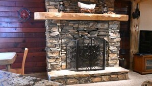 Una chimenea de piedra con repisa de madera, una pared de piedra y un televisor a la derecha.