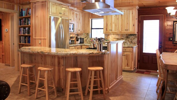 Una cocina de madera con una isla central, taburetes de bar y un refrigerador de acero inoxidable.