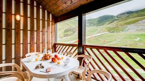 Ein Frühstückstisch mit Croissants, Äpfeln und Saft, mit Blick auf eine gebirgige Landschaft.