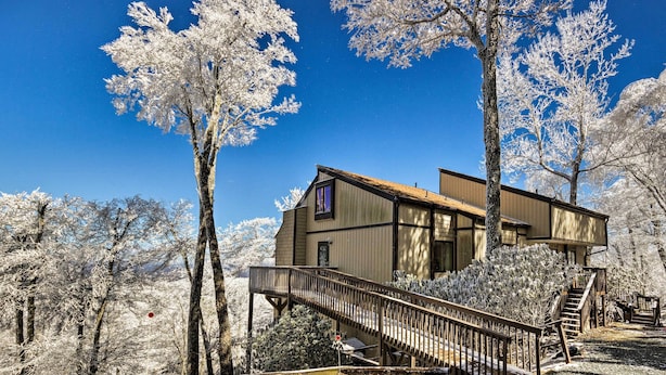 Une cabane en bois avec un escalier menant à une terrasse, entourée d’arbres couverts de neige.