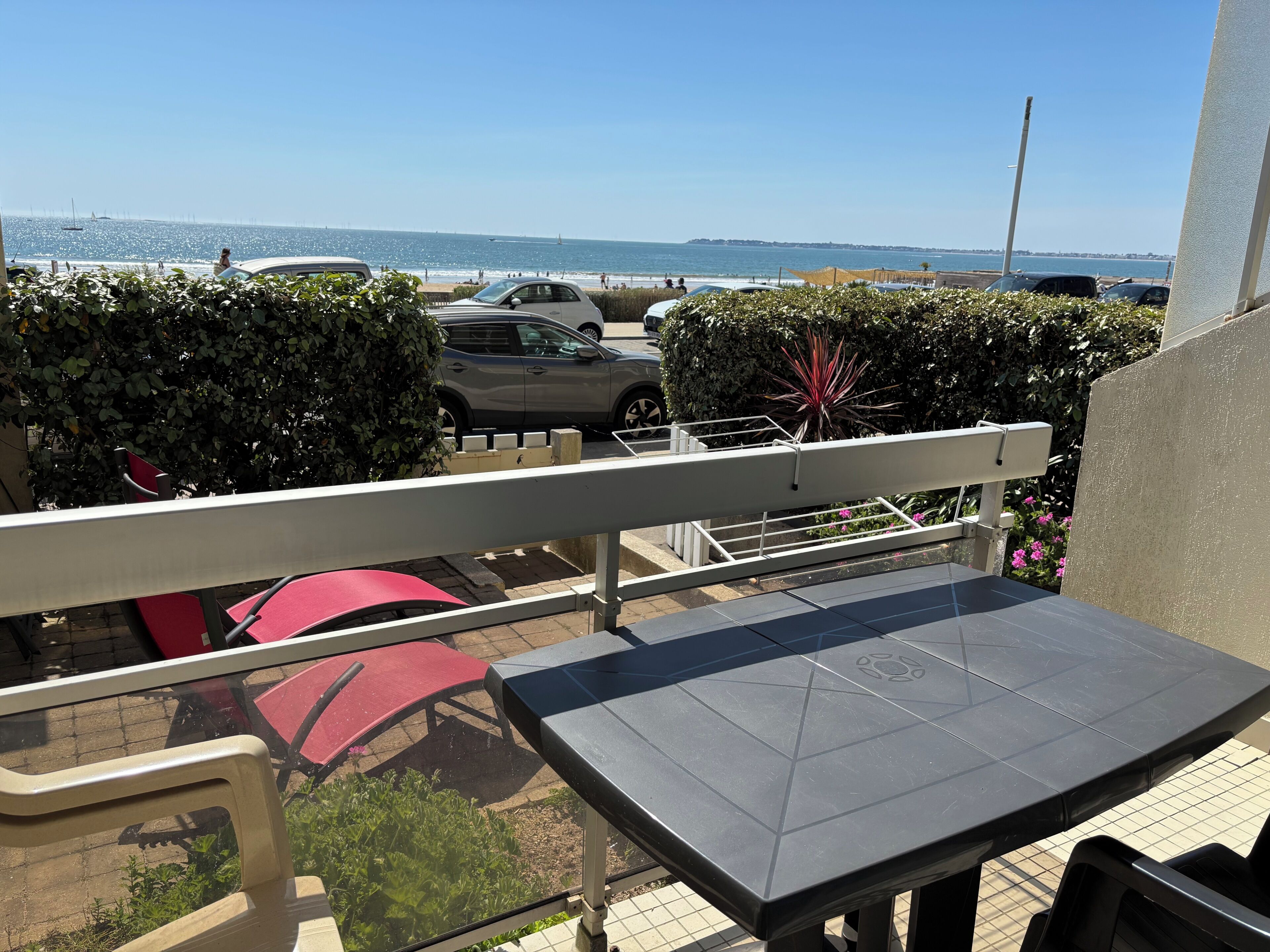 A balcony with a view of the sea, a table, and chairs.