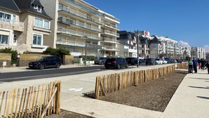 Un edificio residencial de varios pisos con balcones, zona de estacionamiento y acera.