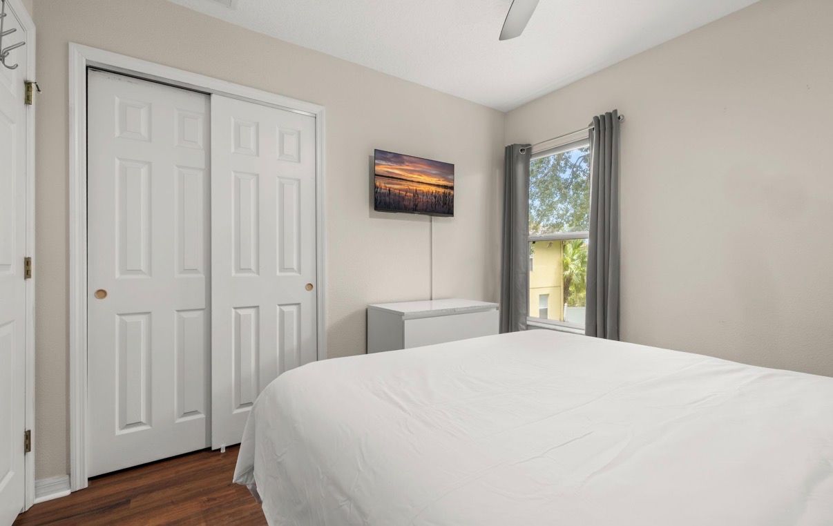 A bedroom with a bed, a white door, a radiator, and a window with curtains.