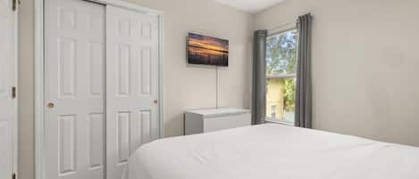 Un dormitorio con cama, una puerta blanca, un radiador y una ventana con cortinas.