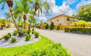 A residential street with palm trees, a yellow building, and a clear sky.
