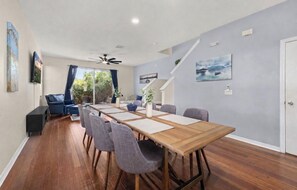 A dining area with a long wooden table, grey chairs, and a ceiling fan.