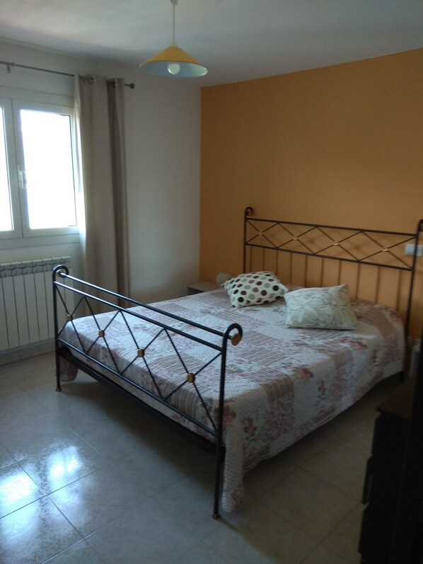 A bedroom with a metal bed frame, a window with curtains, and a radiator.