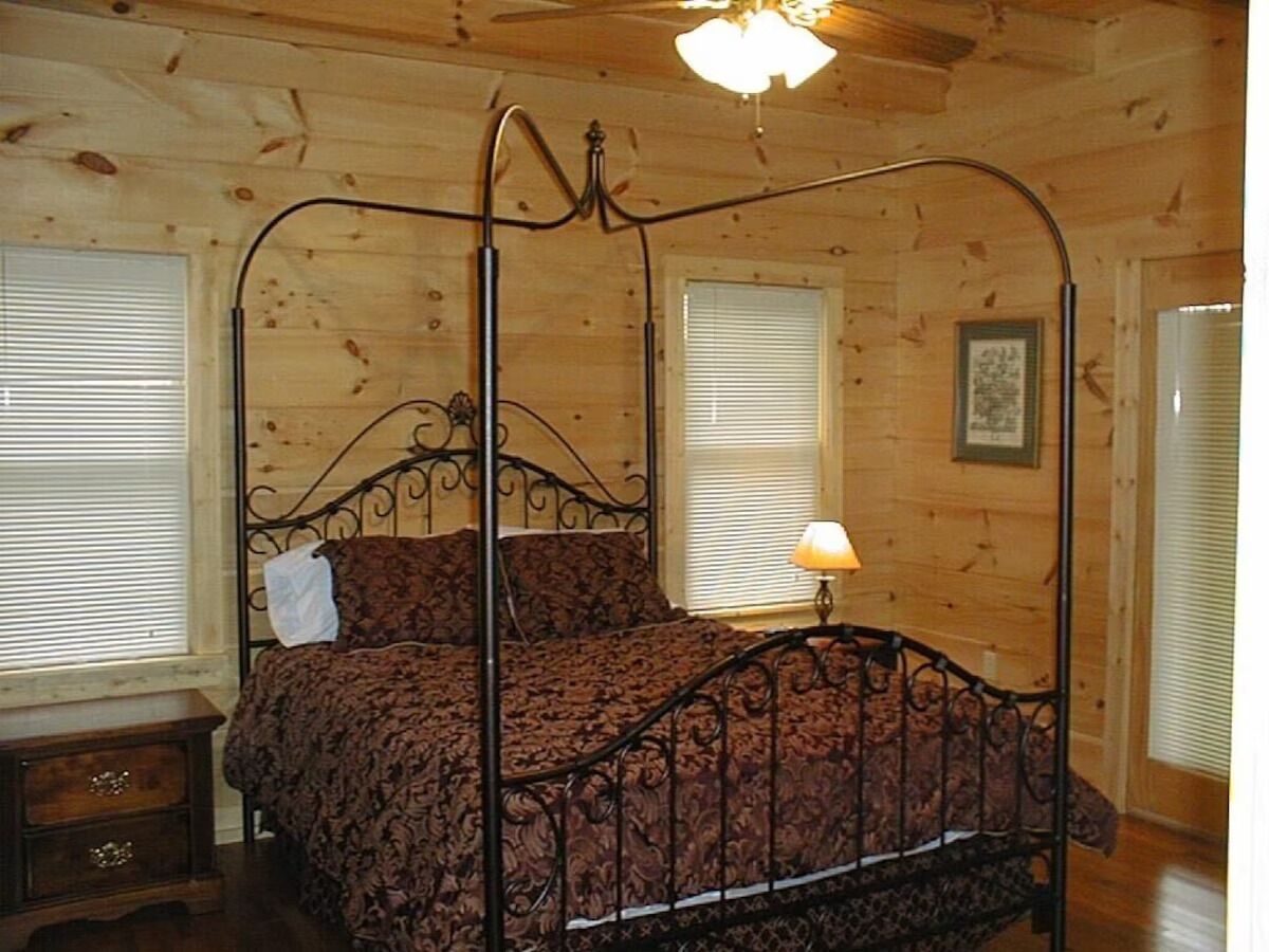 A wooden-paneled bedroom with a four-poster bed, a nightstand, and a ceiling fan.