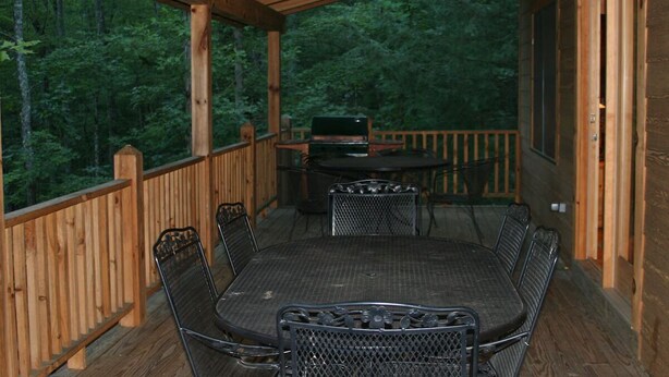 A covered outdoor deck with a dining table and chairs, a grill, and a view of a forested area. - Townsend, Tn & Smoky Mountains! Wooded Privacy & Sleeps 15 (Townsend)
