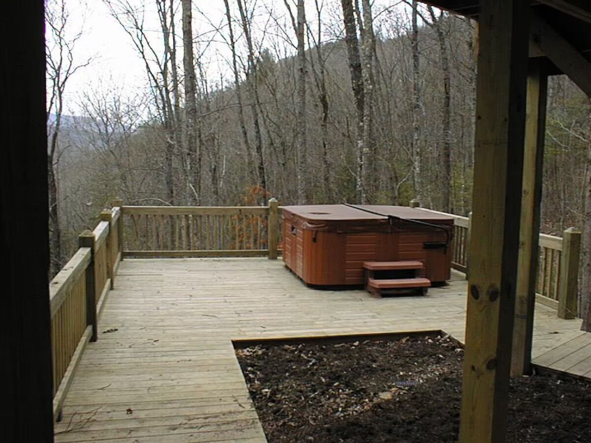 Une terrasse en bois avec un jacuzzi et un banc, entourée d’une clôture en bois et d’arbres.