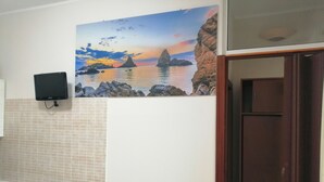 Un baño con pared de azulejos, un cuadro de una escena costera, un televisor montado en la pared y una puerta de madera.