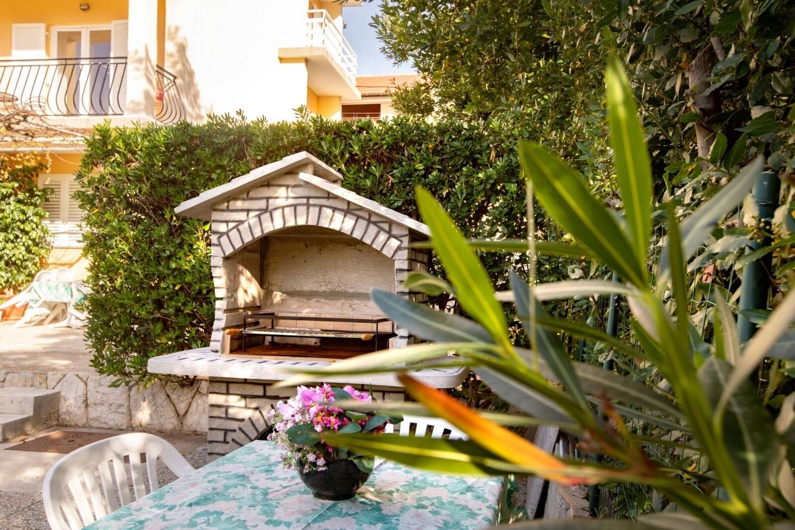 An outdoor brick oven with a table and chairs in front, surrounded by greenery.