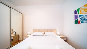 A modern bedroom with a large bed, two bedside tables with lamps, a wooden headboard, and a colorful abstract painting on the wall. - Apartment in Lopar with Terrace, Air condition, WIFI, Washing machine (129-2) (Lopar)