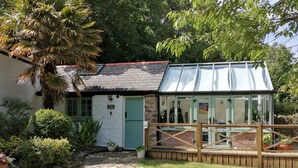 Une charmante maison de campagne avec une porte verte, un chemin de pierres menant à une terrasse en bois et une véranda aux murs de verre.