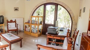 A cozy living room with a wooden sofa, a coffee table, a bookshelf, a television, and a large arched window. - Heliopetra Studios, near beaches (chania)