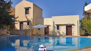 A swimming pool with a table and chairs in front, a building with a stone wall, and a door. - Heliopetra Studios, near beaches (chania)