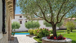 Ein gepflasterter Weg führt zu einem Pool, umgeben von üppigem Grün und blühenden Pflanzen.