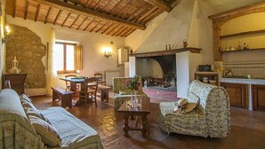 A rustic interior with a stone wall, wooden furniture, a fireplace, and a kitchen area. - Apartment on the first floor with a beautiful panoramic view, Air conditioning. (Torrita di Siena)