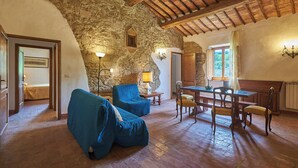 A rustic interior with stone walls, wooden beams, a dining area with a table and chairs, and a blue sofa. - Apartment on the first floor with a beautiful panoramic view, Air conditioning. (Torrita di Siena)