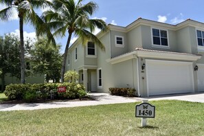 A two-story house with a garage, a front yard with a lawn and palm trees, and a street sign with the number 1450.