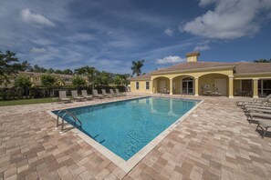 A rectangular pool with a metal ladder, surrounded by a brick patio with lounge chairs.