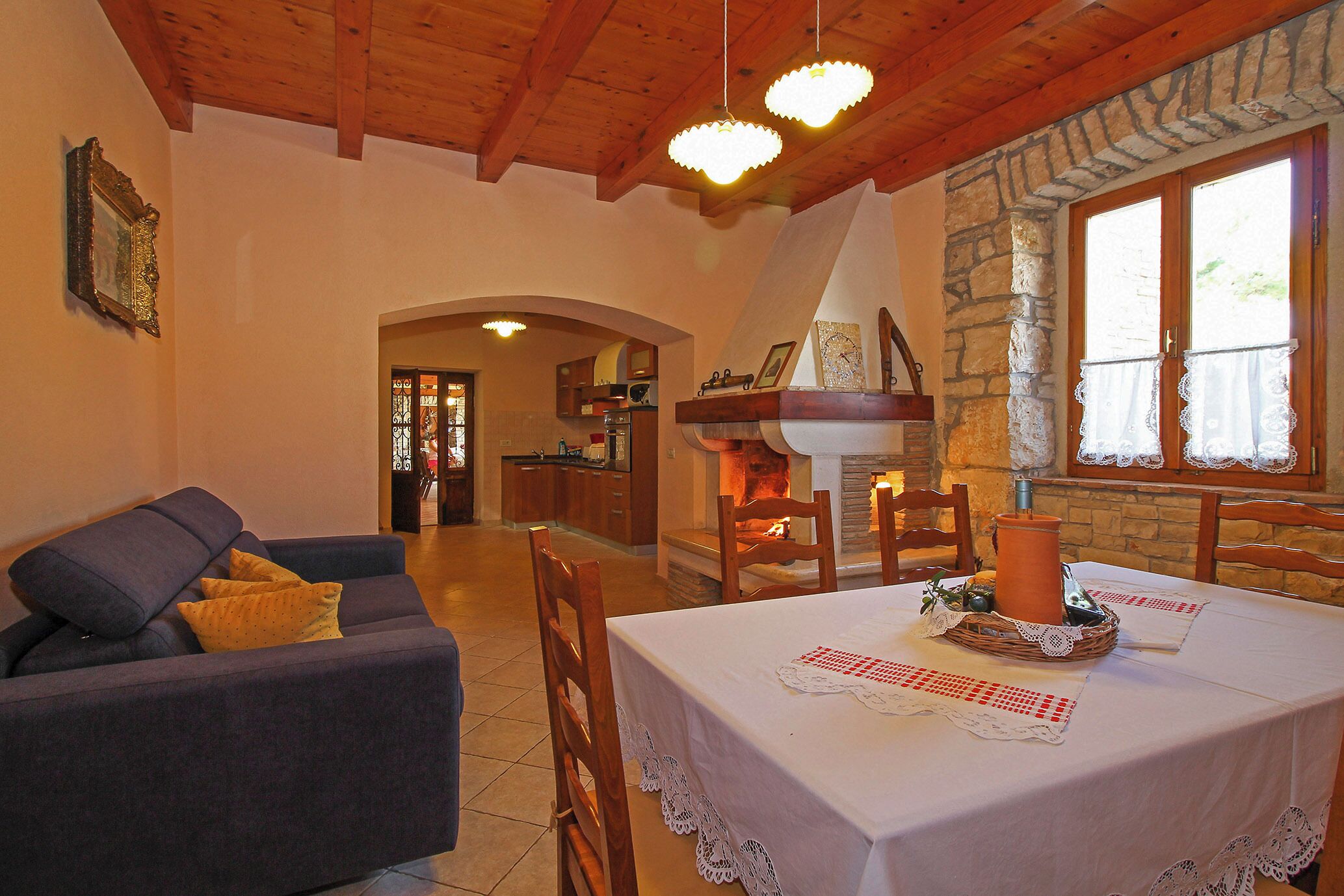 Uma sala de estar acolhedora, com um sofá, uma mesa de jantar posta para dois e uma lareira de pedra.