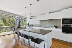 A modern kitchen with a large island, bar stools, and a view of greenery outside. - Bowerbird At Lorne (Lorne)