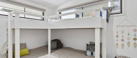 A bunk bed room with a window, a hanging decoration, and a woven rug.