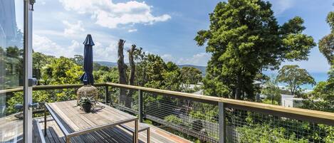 A wooden deck with a metal railing, overlooking a lush landscape with trees and a clear sky.