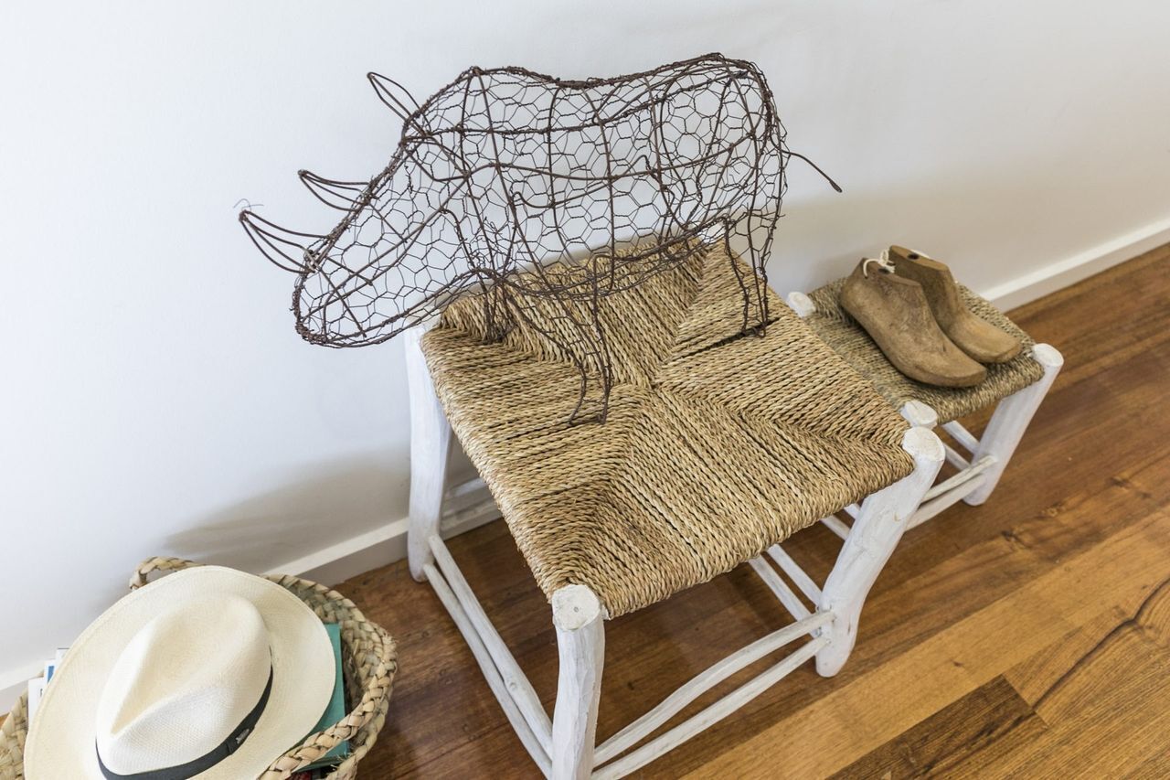 A rustic chair with a woven seat and backrest, accompanied by a pair of brown boots and a straw hat on a wooden floor.