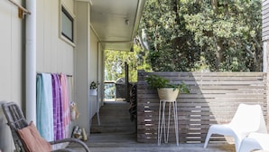 Une terrasse en bois avec des meubles d’extérieur, une plante suspendue et, au loin, la vue d’une maison.