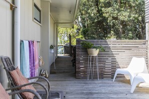 Eine Holzterrasse mit Gartenmöbeln, einer hängenden Pflanze und Blick auf ein Haus im Hintergrund.