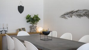 Un espace repas moderne avec une table sombre, des chaises blanches, une plante en pot et des œuvres d’art décoratives accrochées au mur.