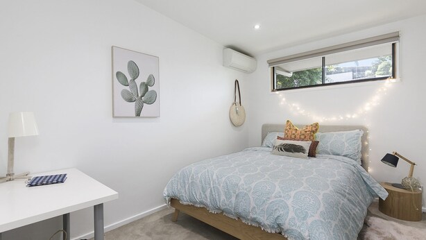 Une chambre à coucher avec un lit, une table de chevet, une lampe et une œuvre d’art représentant un cactus accrochée au mur.