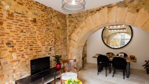 A stone-walled room with a TV, seating, and a dining area with chairs and a table. - Charming apartment in the heart of bergerac (Bergerac)