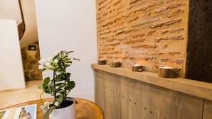 A reception area with a brick wall, a wooden reception desk, a potted plant, and a few candles. - Charming apartment in the heart of bergerac (Bergerac)