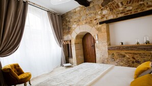 A bedroom with a stone wall, a wooden door, a bed with white bedding, a yellow armchair, and a hanging light fixture. - Charming apartment in the heart of bergerac (Bergerac)