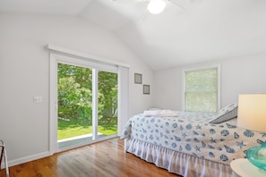 A bedroom with a bed, a window with blinds, a door to a balcony, and a ceiling fan. - ★The Islander | Steps From Water, Fire Pit, AC★ (Mashpee)