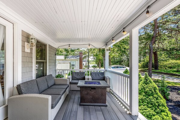 A covered porch with a seating area, a fire pit, and a view of the surrounding greenery and neighborhood. - ★The Islander | Steps From Water, Fire Pit, AC★ (Mashpee)