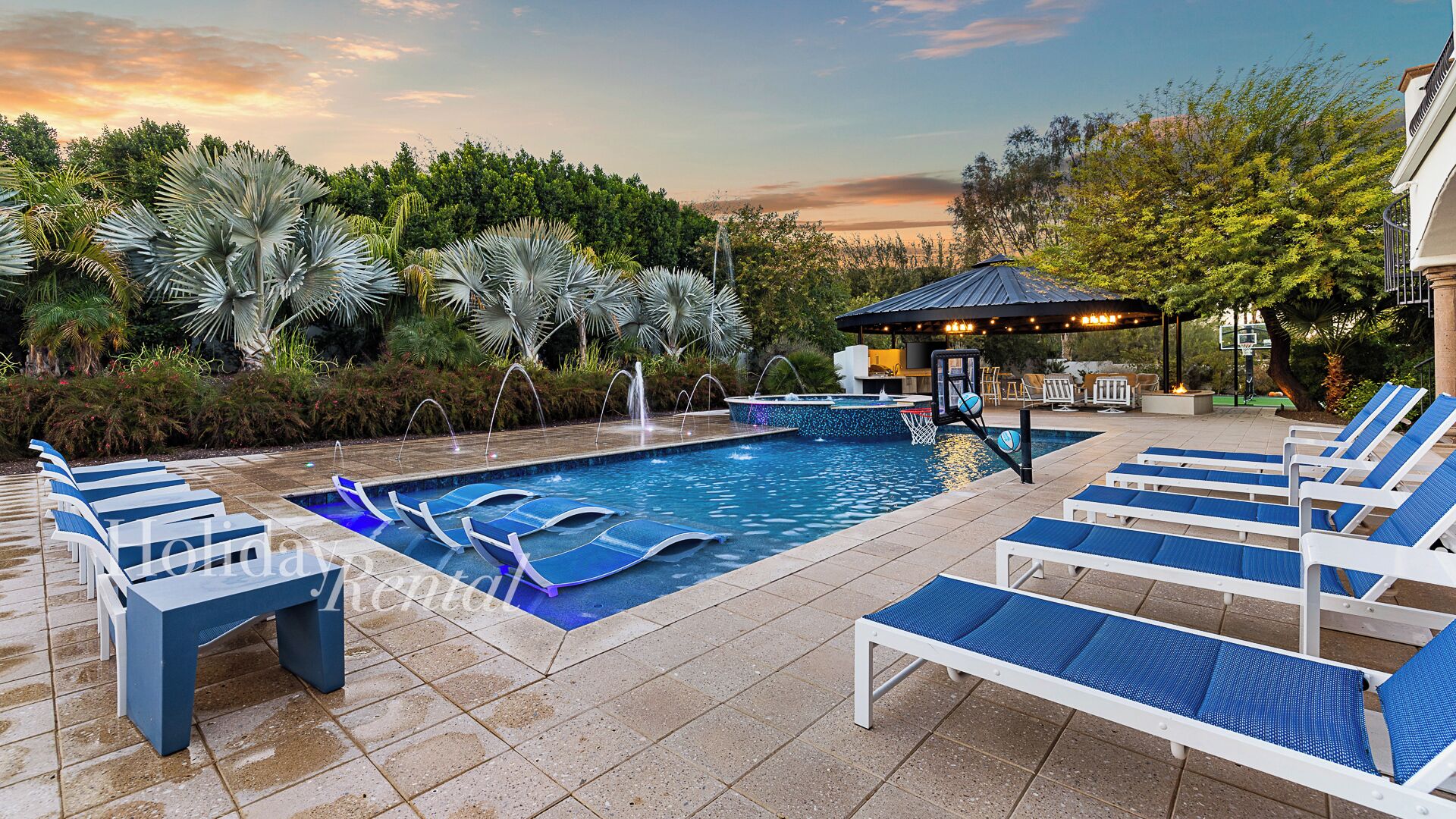 Piscina com espreguiçadeiras, cesta de basquete e um gazebo.