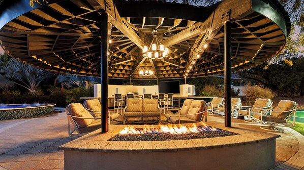 Relax by the fire pit in a cozy outdoor space with comfortable seating and a flat-screen TV.