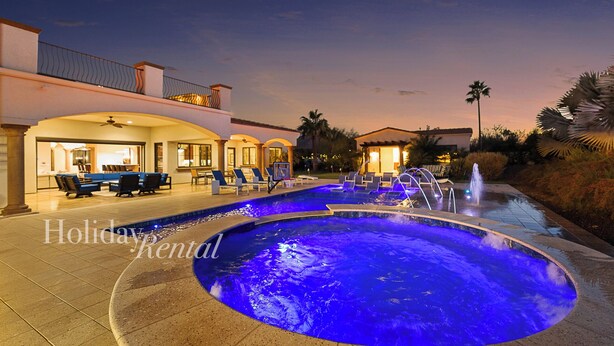 Piscina con illuminazione blu, area relax esterna e un edificio con patio.