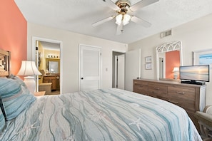 A bedroom with a bed, dresser, television, and a ceiling fan.