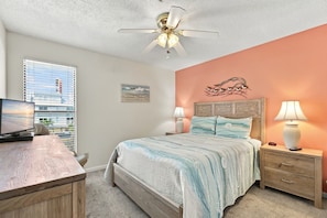 A bedroom with a bed, bedside tables, a desk, a television, and a ceiling fan.