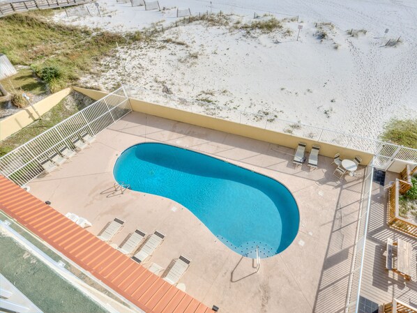 An aerial view of a swimming pool with a curved edge, surrounded by a deck with lounge chairs and a small table.